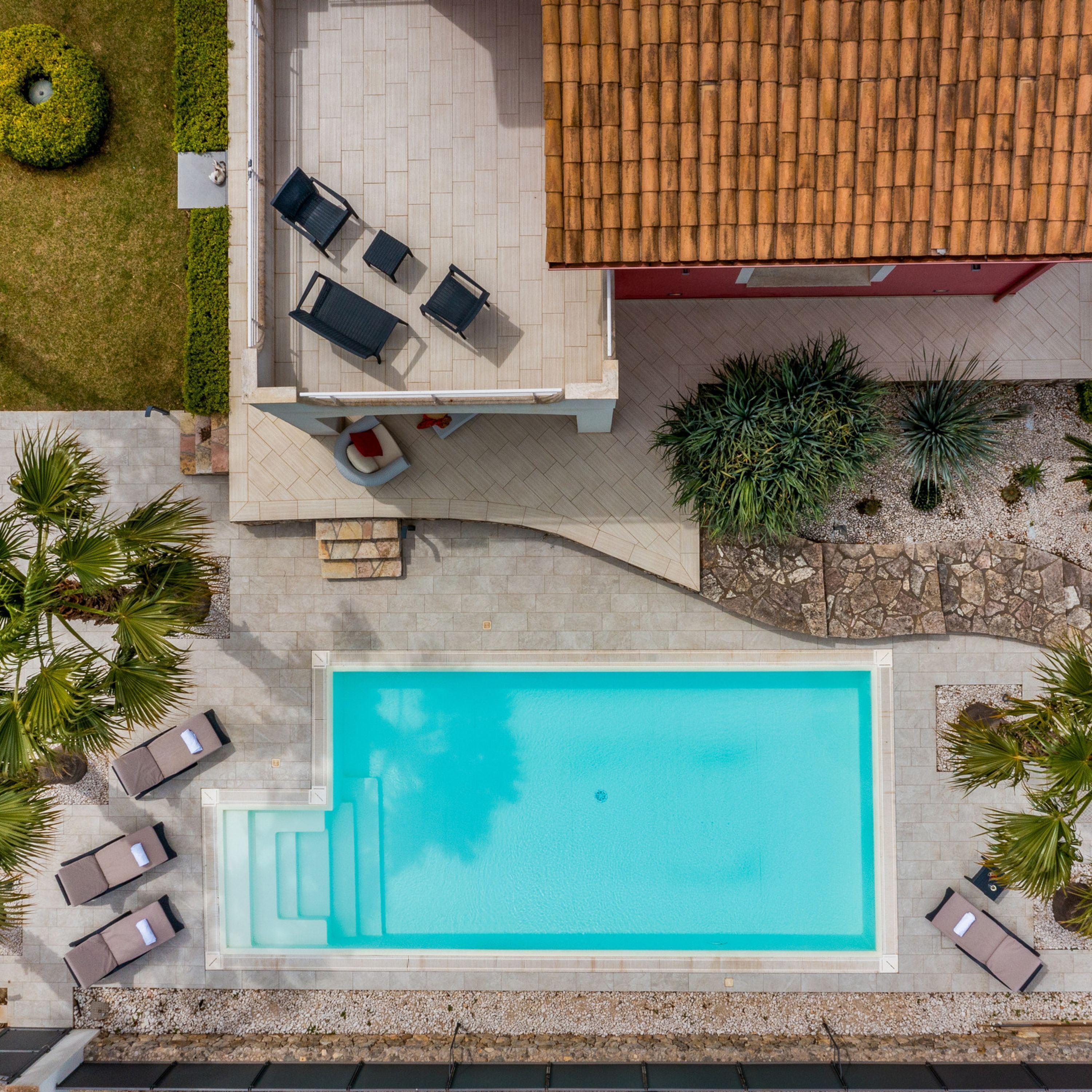 An aerial view of a swimming pool area with lounge chairs, a small seating area, and surrounding landscaping.