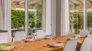 A dining area with a wooden table, white chairs, and glass doors leading to a garden. - Villa Jacqueline con Piscina Privata 8 Posti Letto (Castellammare del Golfo)