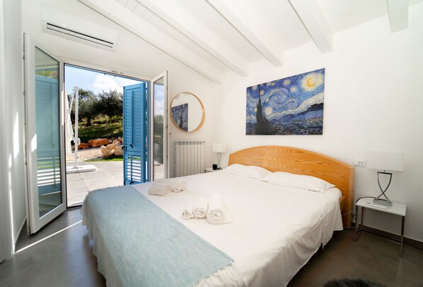 Un dormitorio con cama, un cuadro, un espejo redondo y vistas al exterior.