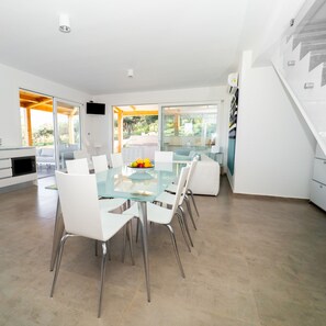 A modern kitchen with a glass dining table, white chairs, and a fruit bowl. - Villa Majestatis in Scopello (Castellammare del Golfo)