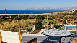 A terrace with a table and chairs, overlooking a pool and a scenic view of the sea and hills. - Villa Majestatis in Scopello (Castellammare del Golfo)