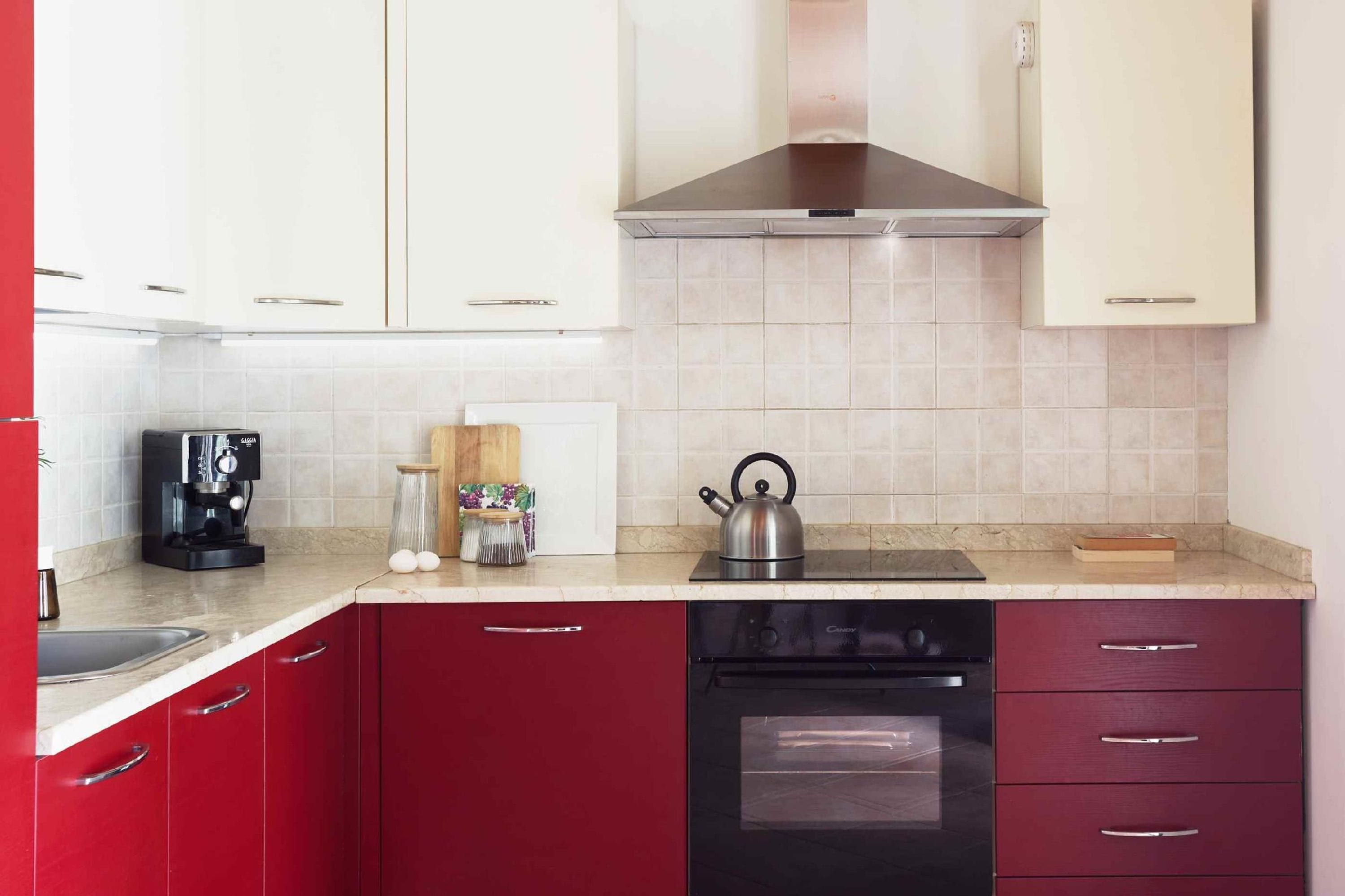 Une cuisine avec des meubles de couleur rouge, une hotte de cuisinière en acier inoxydable, une machine à café, une bouilloire et un lave-vaisselle.