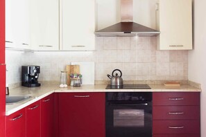 A kitchen with red cabinets, a stainless steel range hood, a coffee maker, a kettle, and a dishwasher. - Giardino di Limoni Eco Friendly Villa (Noto)