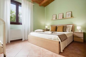 A bedroom with a bed, bedside tables, a window with curtains, and wall-mounted picture frames. - Giardino di Limoni Eco Friendly Villa (Noto)