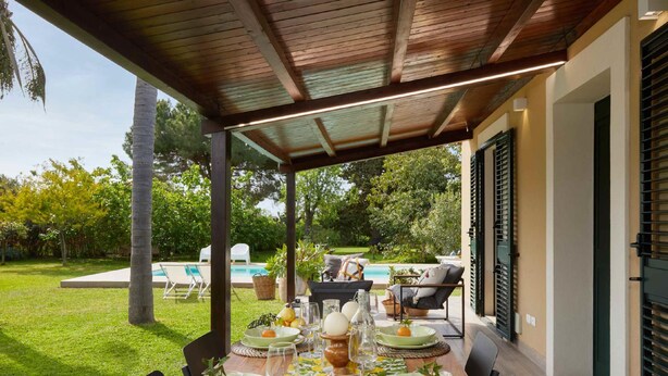 An outdoor dining area with a covered patio, a pool, and a garden view. - Giardino di Limoni Eco Friendly Villa (Noto)