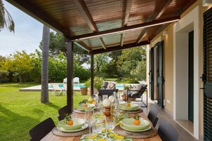 Un área de comedor al aire libre con un patio cubierto, una piscina y vistas a un jardín.