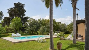 A swimming pool with lounge chairs and a hammock, surrounded by palm trees and greenery. - Giardino di Limoni Eco Friendly Villa (Noto)