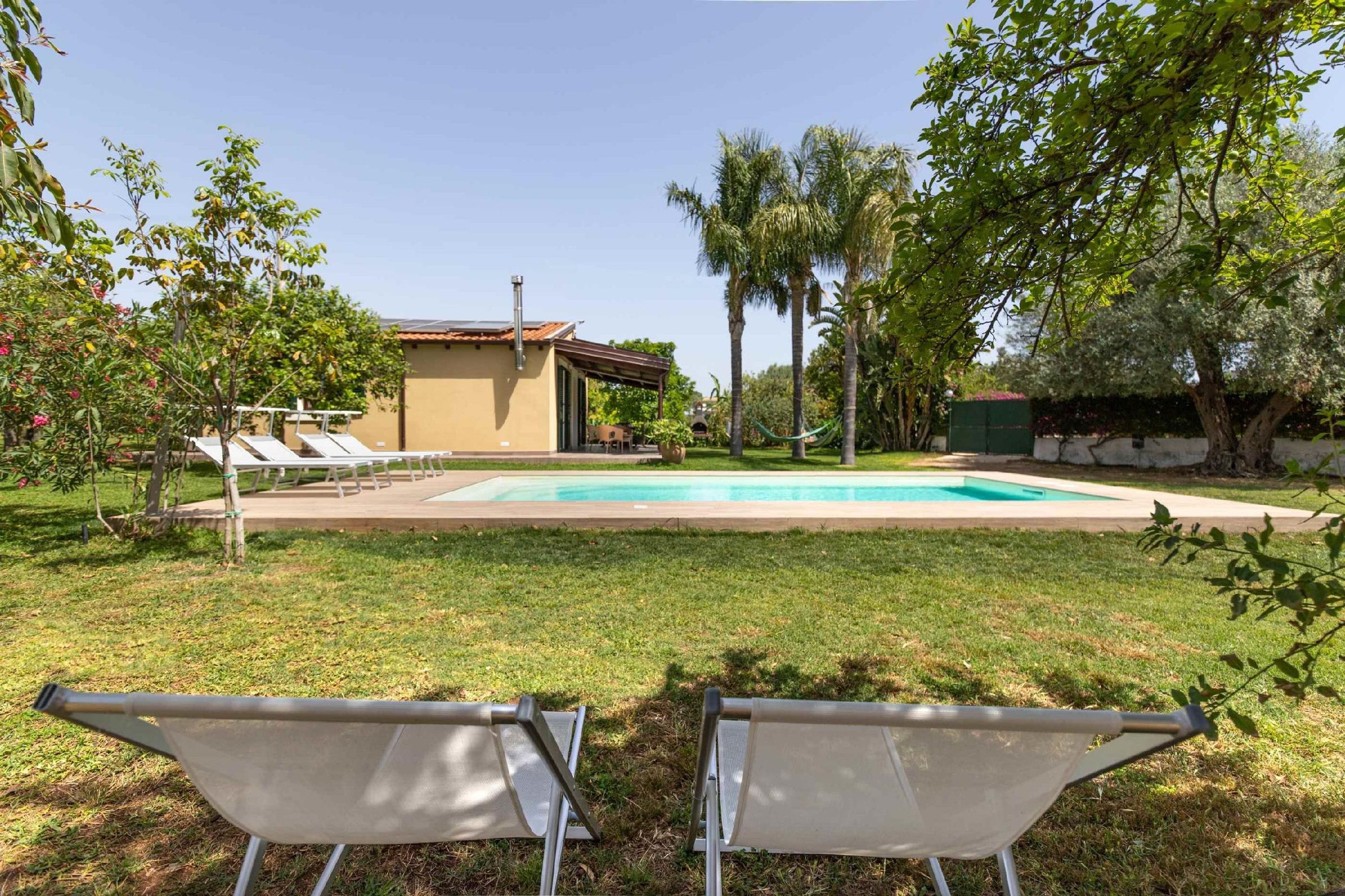 A backyard with a swimming pool, lounge chairs, and a house.