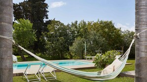 A hammock by a pool with a grassy area and trees in the background. - Giardino di Limoni Eco Friendly Villa (Noto)