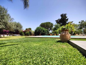 A well-maintained grassy area with a large planter and a pool in the background. - Giardino di Limoni Eco Friendly Villa (Noto)