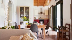 A spacious room with a wooden ceiling, a dining area with a table and chairs, a kitchen with red cabinets, and a large window. - Giardino di Limoni Eco Friendly Villa (Noto)