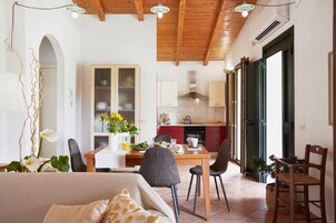 Una habitación amplia con techo de madera, un comedor con mesa y sillas, una cocina con armarios rojos y un ventanal grande.