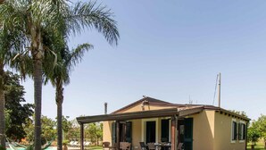 Una casa de un piso con un porche cubierto, una piscina y palmeras en el jardín.
