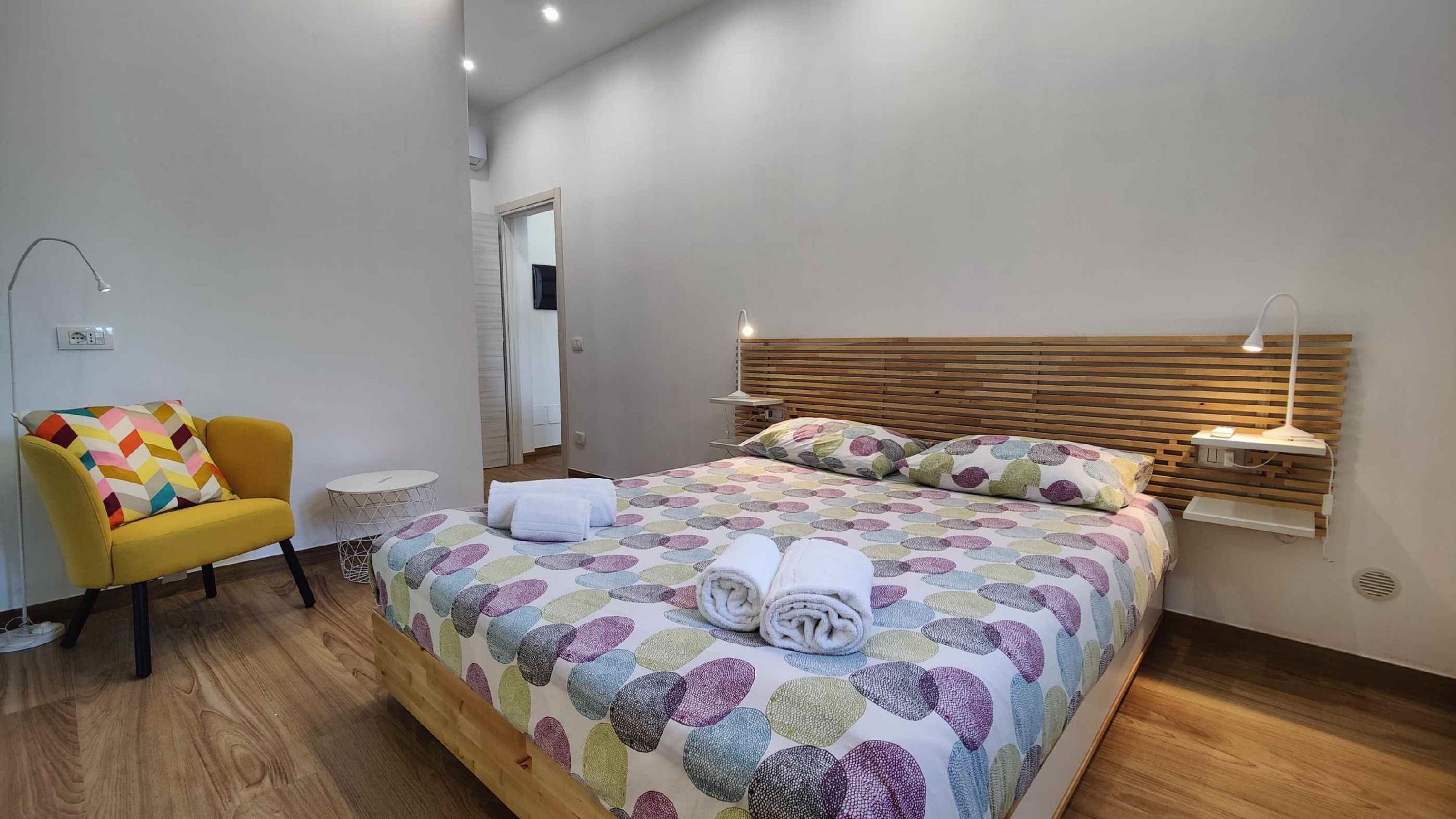 A modern bedroom with a wooden bed, a yellow armchair, a round side table, and a bedside lamp.