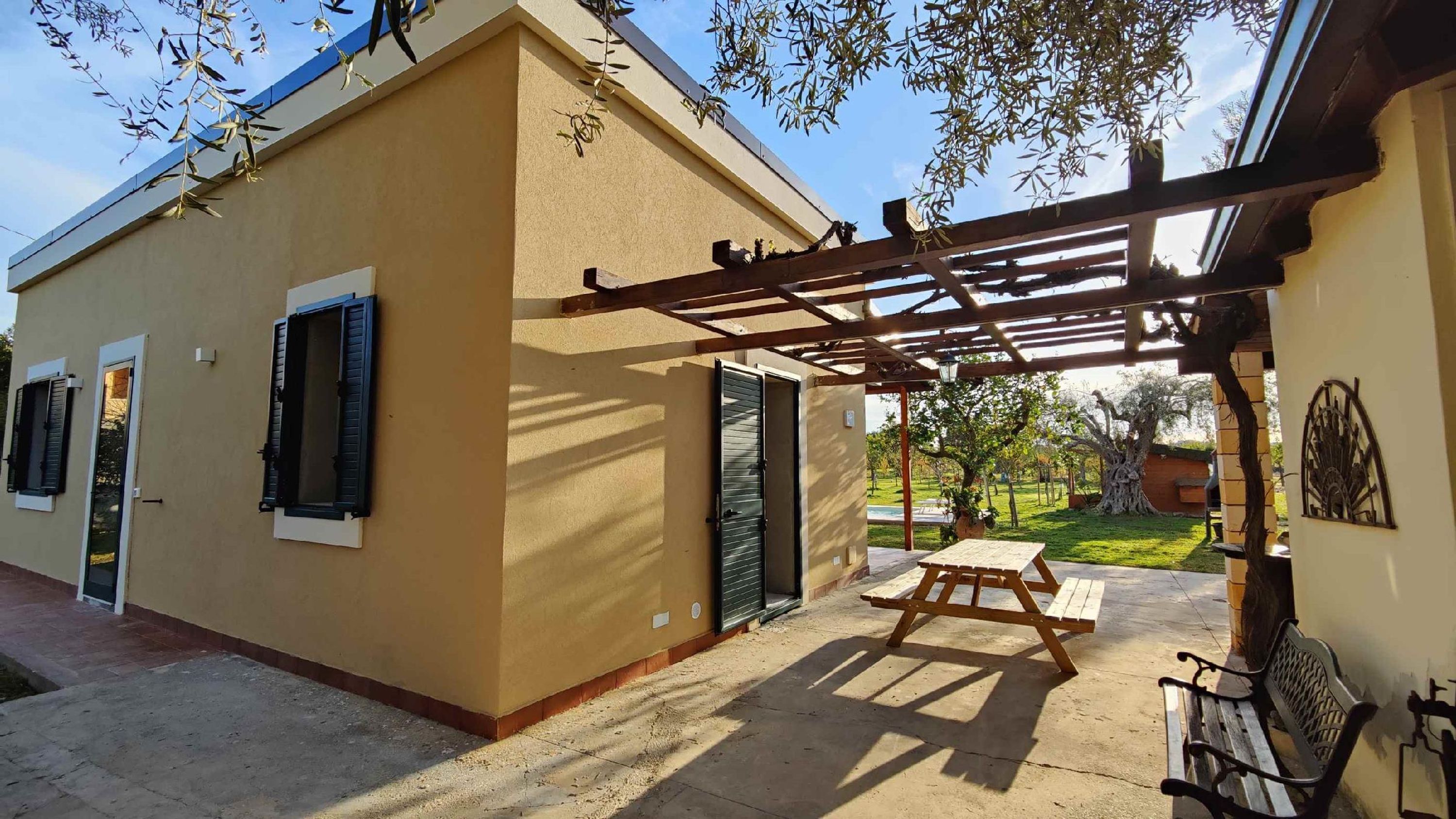 Een gebouw met een terras, een pergola en een bank.