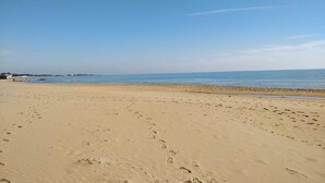 Ein weiter Sandstrand mit Fußspuren, die zum Wasser führen.