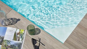 A poolside view with a magazine, sunglasses, and a hat on a wooden deck.