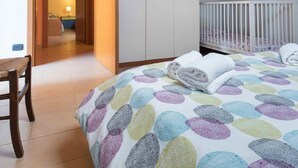 A bedroom with a bed, a crib, a wardrobe, and a door leading to another room. - Apartment Eucaliptus sea View (Avola)