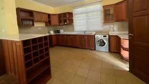 Une cuisine avec des meubles de rangement en bois, un meuble à vin intégré, un lave-linge et une fenêtre avec des stores.