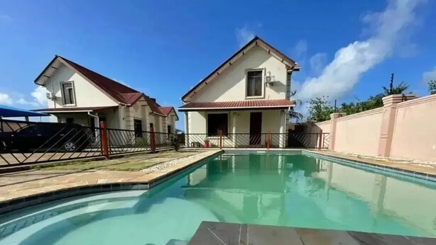 Une propriété résidentielle dotée d’une piscine, de deux maisons et d’une entrée sécurisée par un portail.