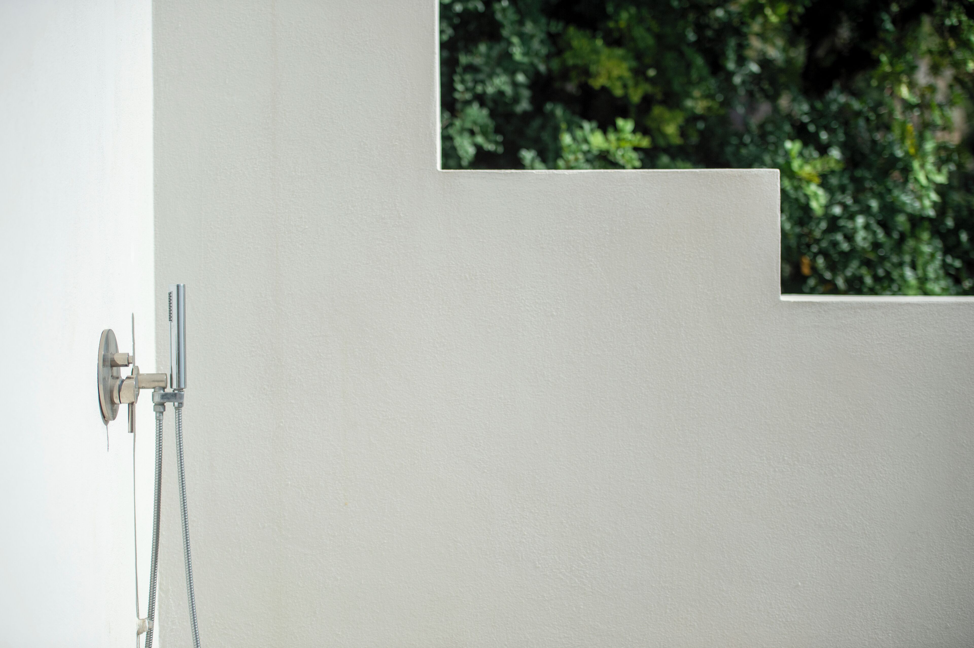 A bathroom with a shower, a small window, and a white wall.