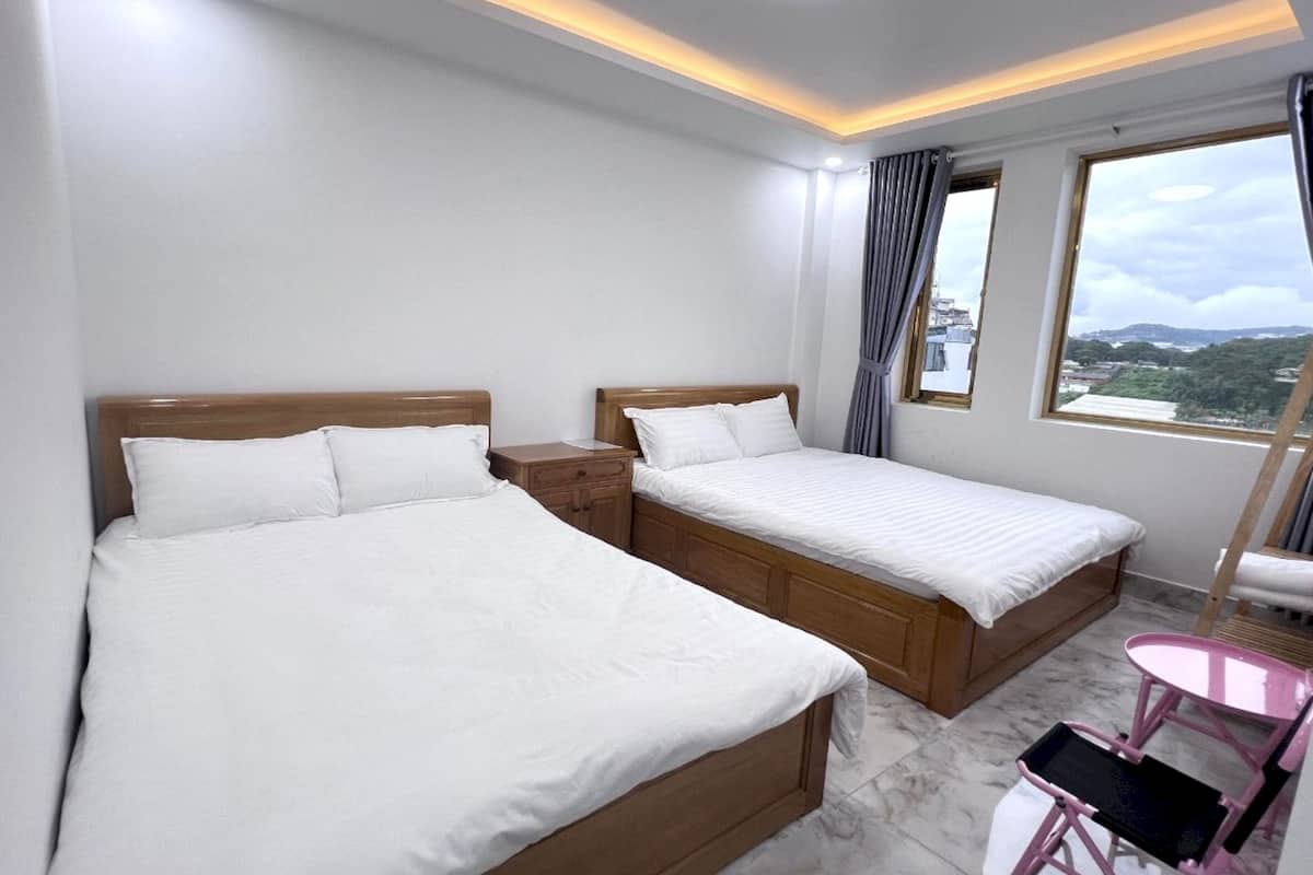 A hotel room with two beds, a small table, a chair, and a window with a view of the city.
