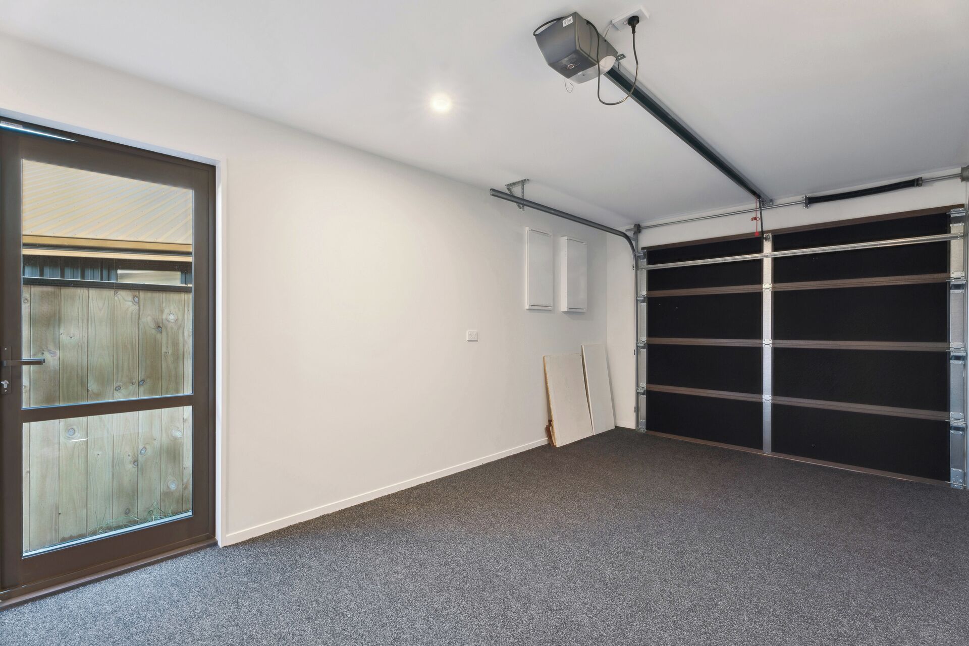 Un garage doté d’une grande porte, d’un luminaire fixé au plafond et d’une porte de garage noire.