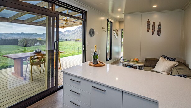 Une cuisine moderne dotée d’un grand îlot central, de portes-fenêtres coulissantes donnant sur une terrasse et offrant une vue sur un paysage verdoyant.