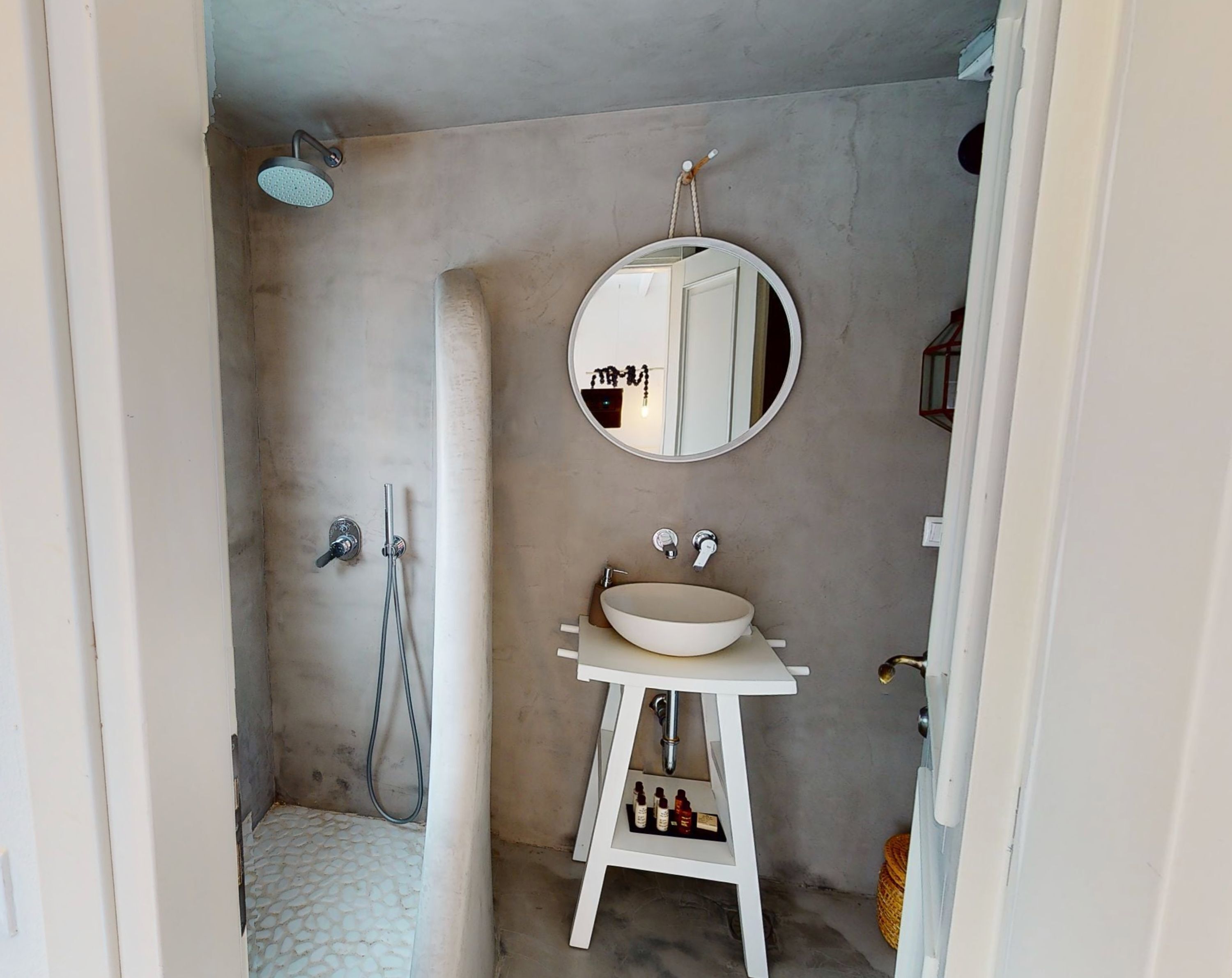 A bathroom with a white pedestal sink, a round mirror, and a shower area.
