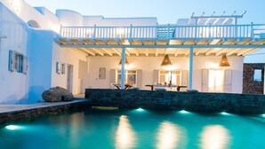 Una villa moderna con piscina, muros de piedra y un espacio al aire libre techado con asientos.