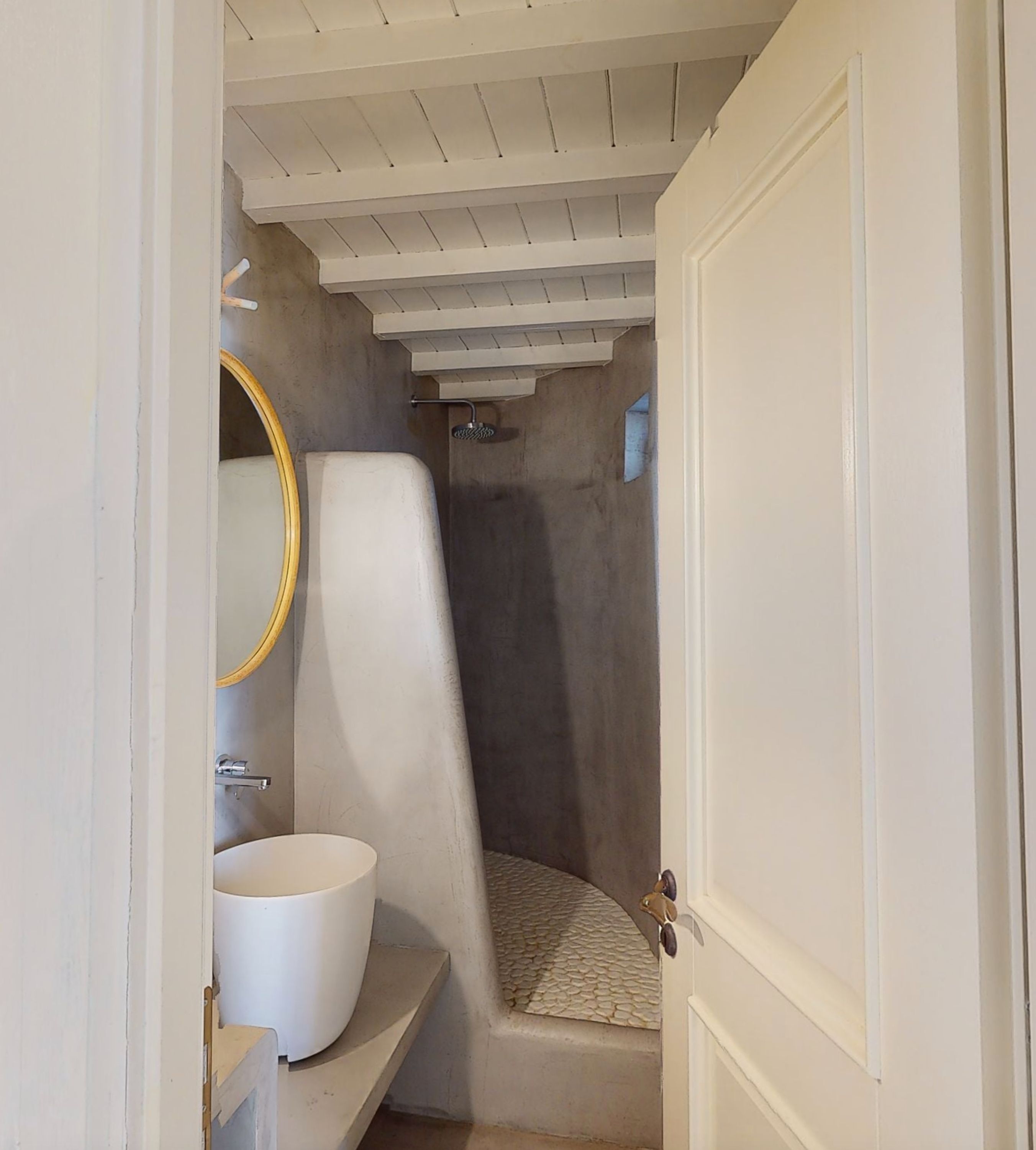 Ett badrum med ett vitt handfat, en rund spegel och en duschhörna.
