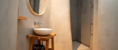 A bathroom with a round mirror, a white sink on a wooden stool, and a shower area.