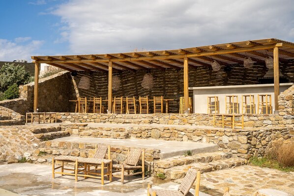 Un bâtiment en pierre doté d’une pergola en bois et d’un espace extérieur aménagé pour s’asseoir.