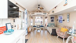 Il s’agit d’un espace de vie compact comprenant un coin cuisine, un coin repas et un coin salon. Il est équipé d’un ventilateur de plafond, d’une table à manger avec des chaises, d’un canapé agrémenté de coussins à motifs et d’une petite table d’appoint.