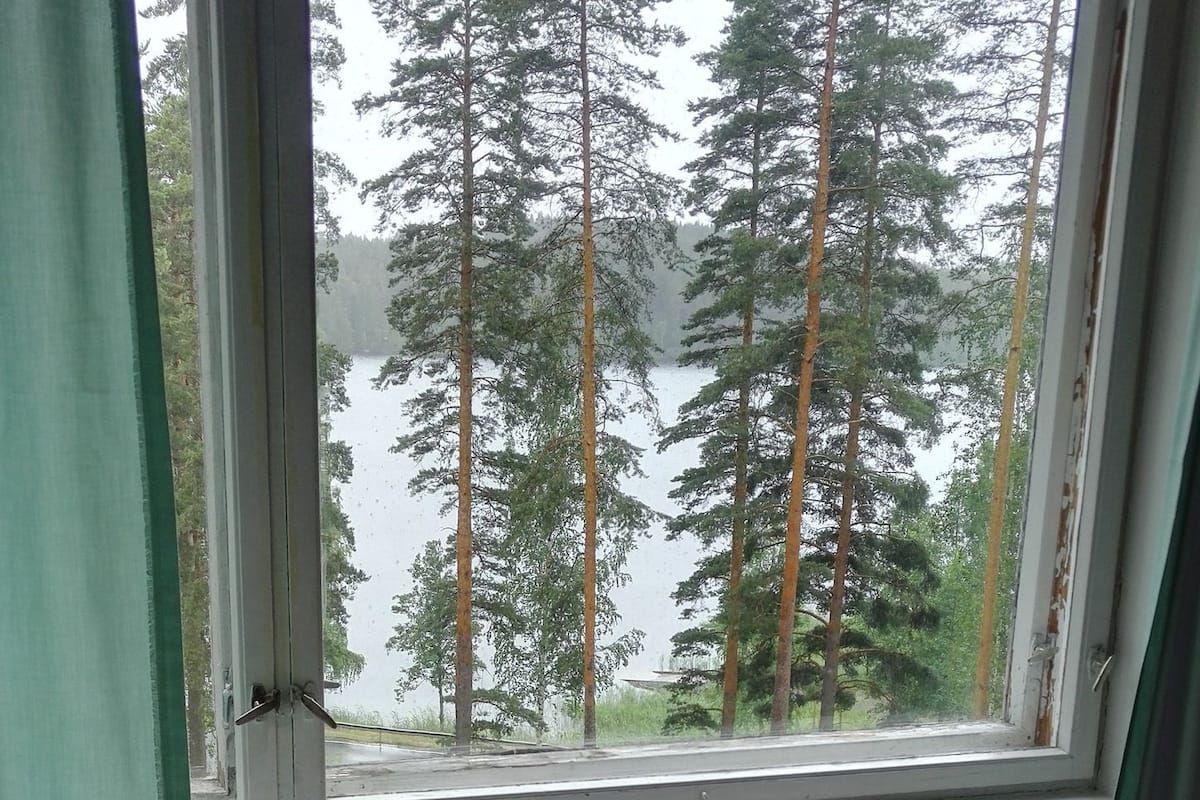 A bedroom with a window overlooking a forest and a body of water.