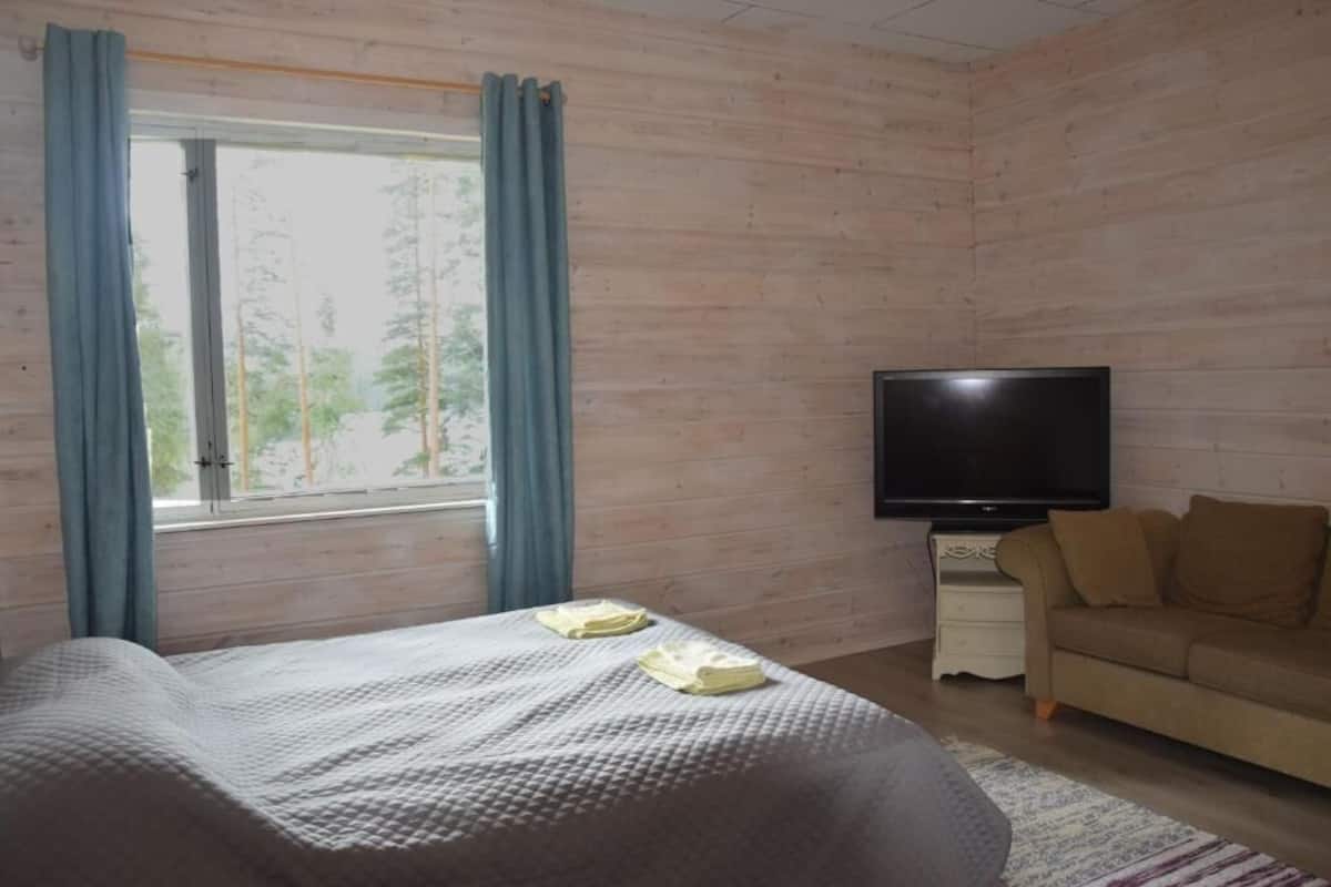 A bedroom with a bed, a TV, a sofa, and a window with curtains.