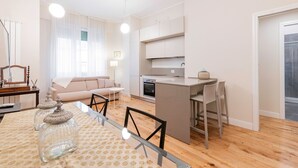 A modern kitchen with a central island, a dining area with a glass table, and a living room with a sofa and a TV. - Appartamento Tiepolo Elegant Venue in Porta Venezia (Milan)
