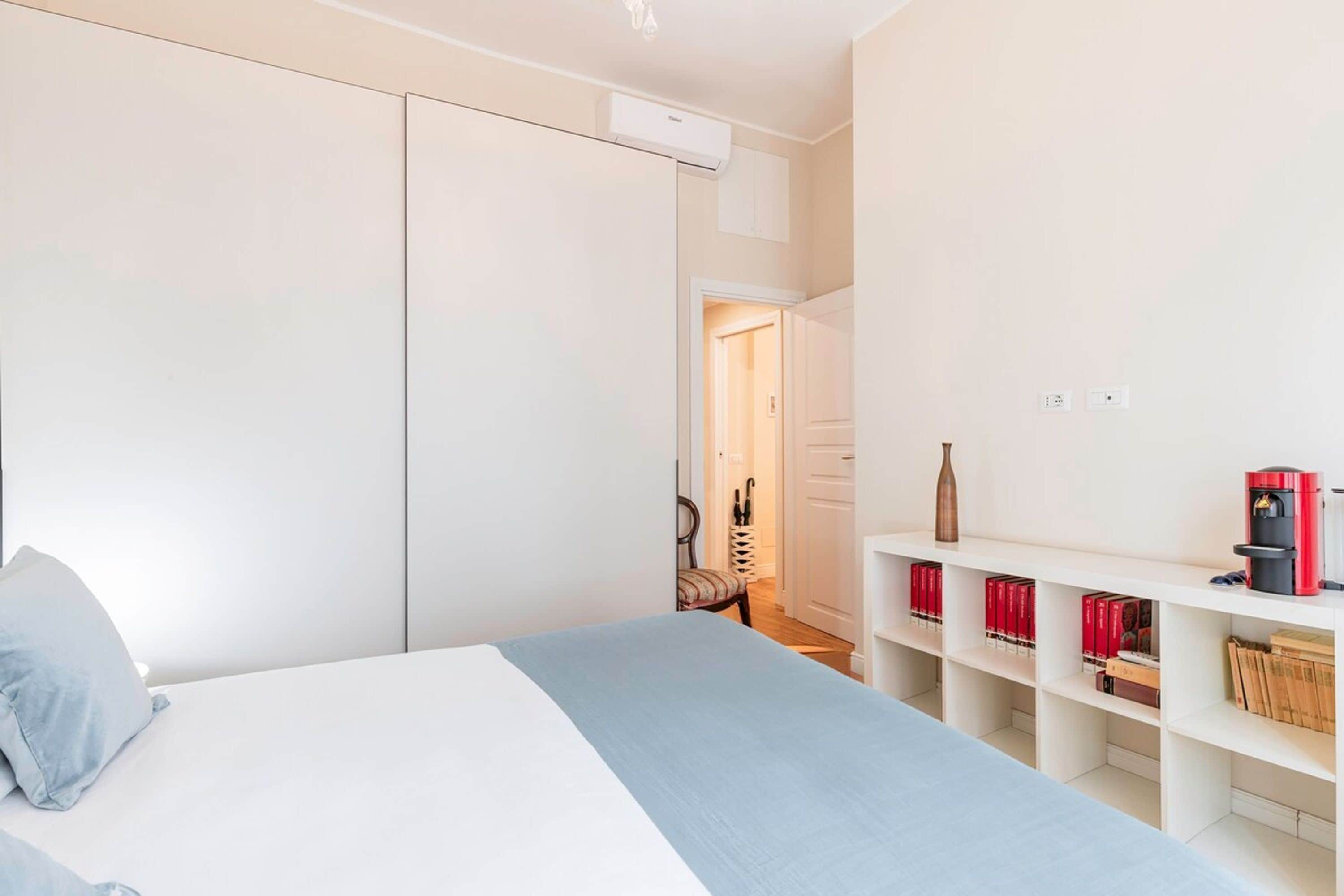 Un dormitorio con cama, armario, estantería con libros y equipo de aire acondicionado.