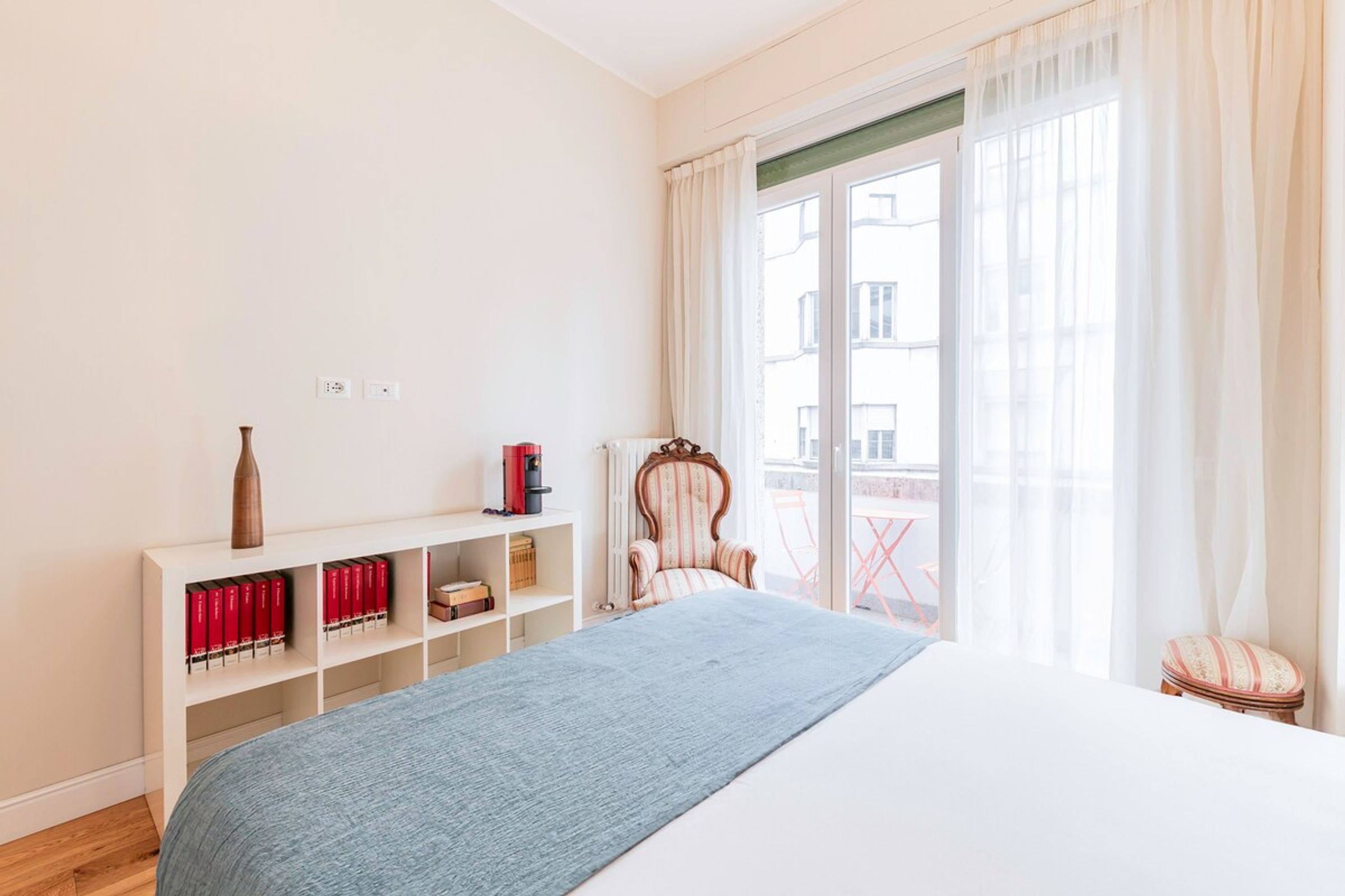 Une chambre à coucher avec un lit, une armoire blanche, une chaise et une fenêtre avec des rideaux.