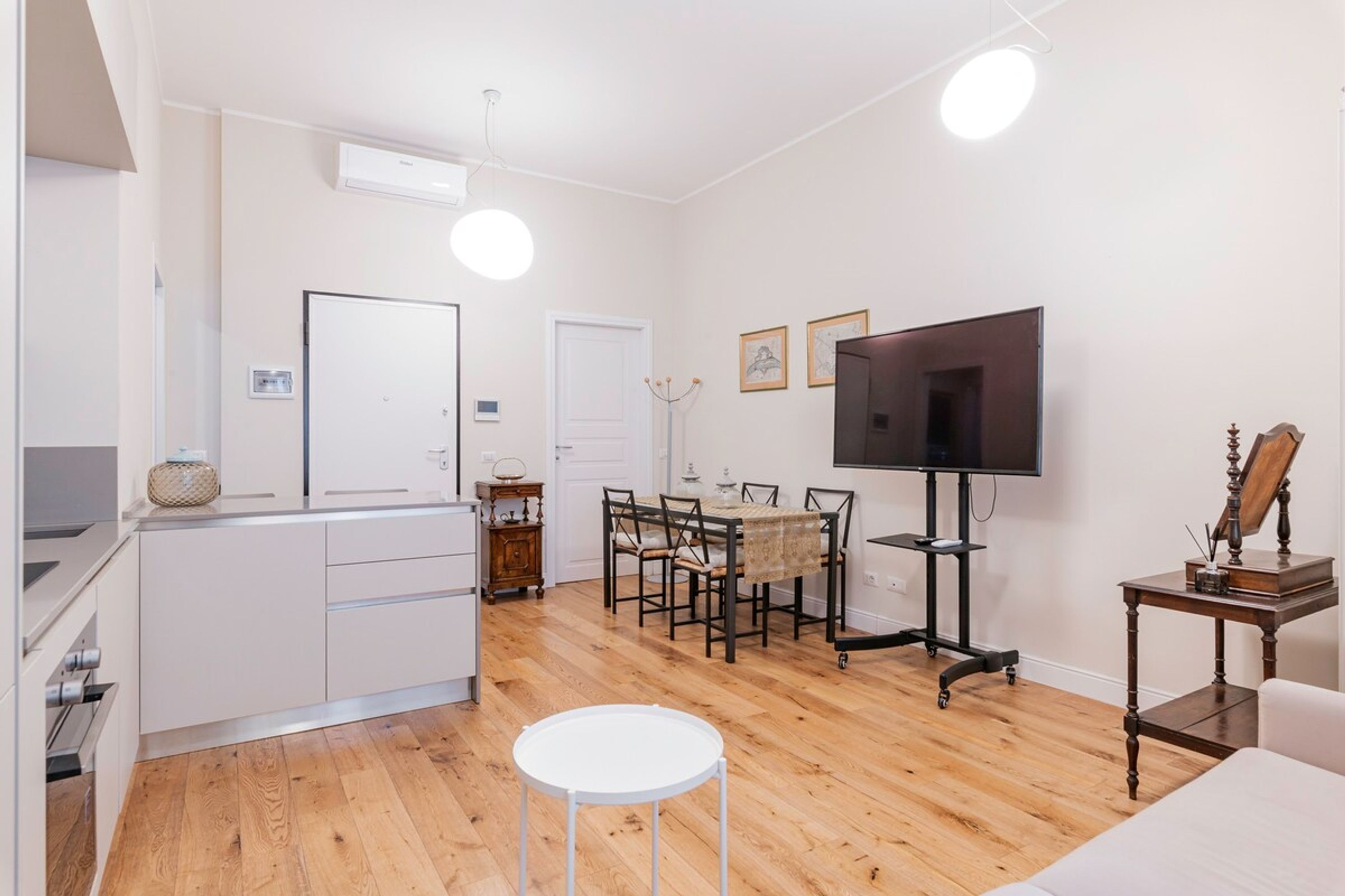 A modern, well-lit room with a dining area, a TV, and a small table with a lamp.
