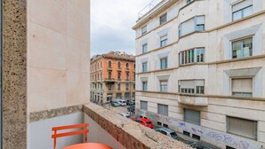 A balcony with a red chair and a table, overlooking a street with parked cars and buildings. - Appartamento Tiepolo Elegant Venue in Porta Venezia (Milan)