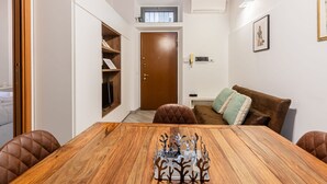 Un coin repas avec une table et des chaises en bois, un canapé en cuir marron et une petite fenêtre au-dessus de la porte.