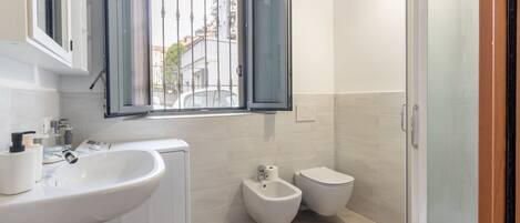 A modern bathroom with a large sink, bidet, toilet, and a window with bars.