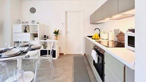 A modern kitchen with white cabinetry, a dining area with clear chairs and a table set for four, and a small island with a sink and a microwave. - Moderno Bilocale con Terrazzo e Parcheggio (Florence)