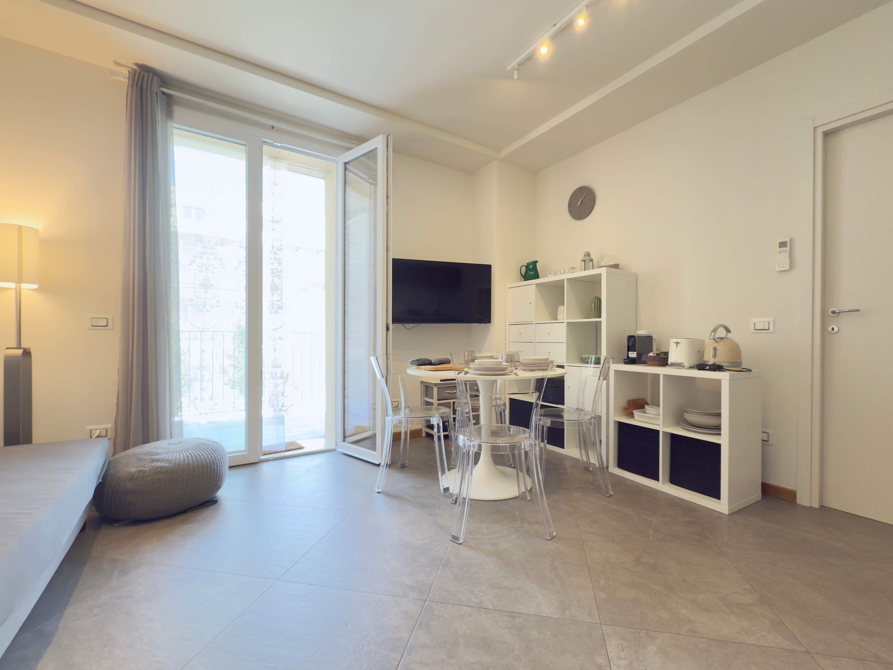 Una sala de estar moderna con sofá, una mesa de comedor con sillas, un televisor montado en la pared y una zona de cocina con armarios y electrodomésticos.
