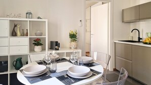 A modern dining area with a round table set for four, clear chairs, and a white cabinet with shelves. - Moderno Bilocale con Terrazzo e Parcheggio (Florence)