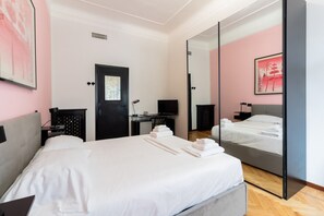 Une chambre d’hôtel avec un grand lit, un bureau avec un ordinateur, une chaise, une porte noire, un miroir et un mur orné d’un tableau.