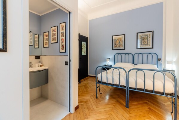 Une chambre à coucher avec un lit en métal, une table de chevet et un mur orné de tableaux.