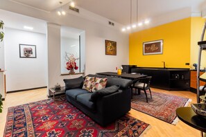 Un salon moderne avec un canapé noir, une table à manger et un coin cuisine.