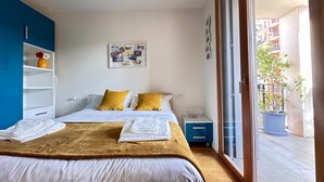 A bedroom with a bed, a nightstand, a blue wardrobe, a wall with photos, and a balcony with a potted plant. - Stylish Apartment With Terrace and Swimming Pool (Milan)